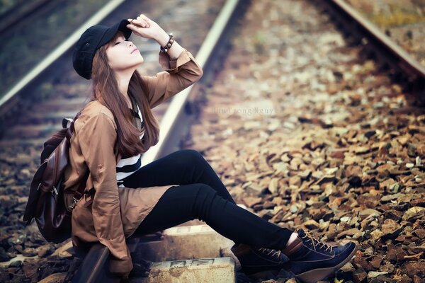 Ragazza asiatica in un berretto si siede sui binari del treno