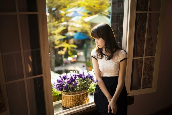 Asiatische Mädchen am Fenster mit lila Blumen