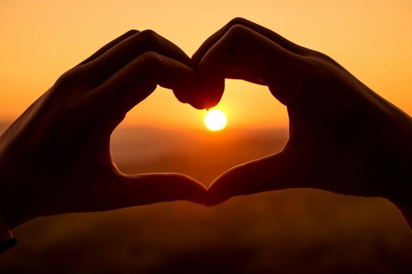 Mains de la jeune fille en forme de coeur sur fond de coucher du soleil
