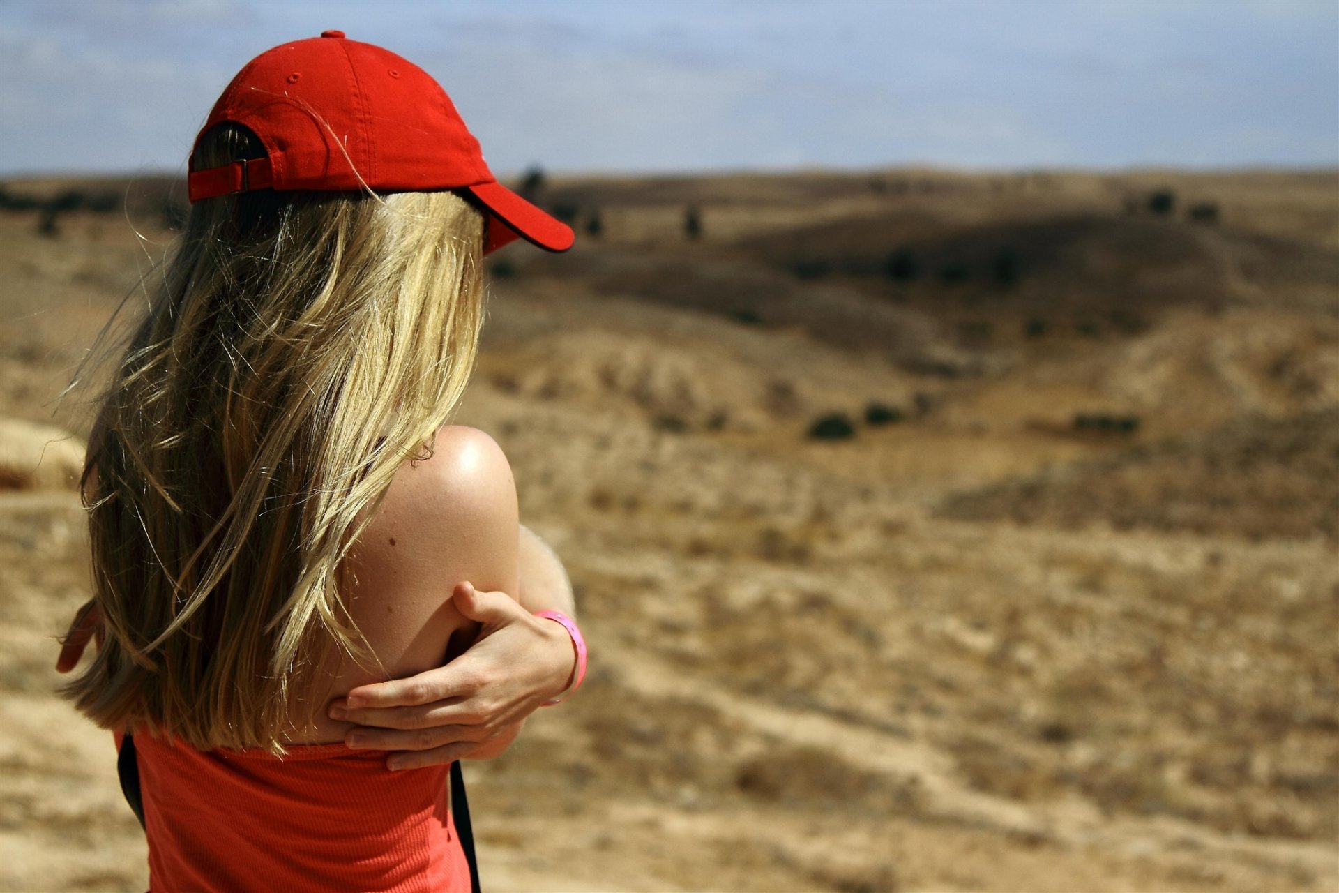 mädchen blond rot kappe t-shirt schultern hände ferne hügel