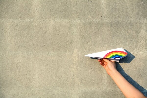 Paper airplane with a rainbow wing on a white wall background
