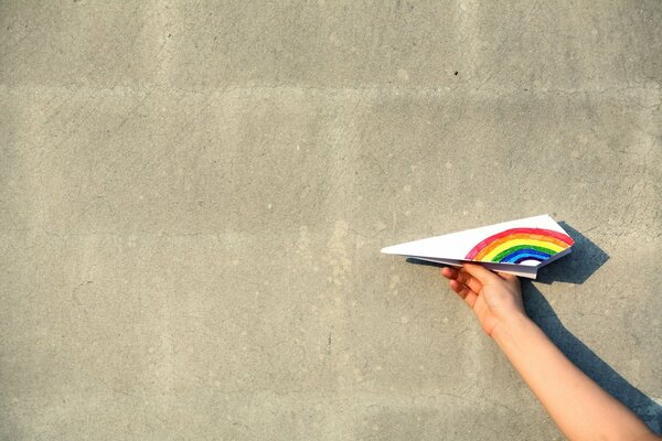 Aeroplano di carta con ala arcobaleno su sfondo muro bianco