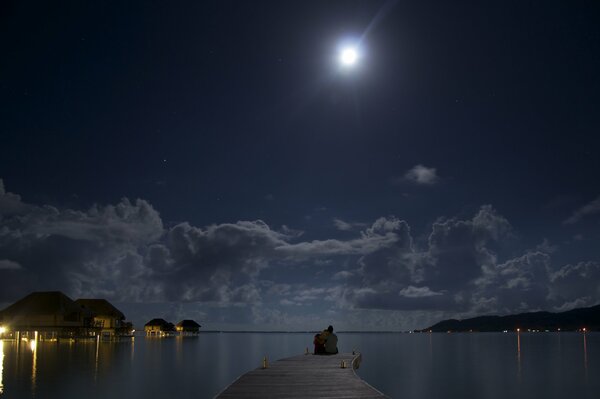 Two people on the seashore look at the moon