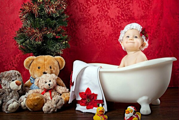 A baby in a cap is sitting in a bath surrounded by toys