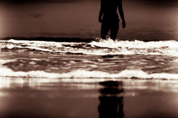 Female silhouette going to the sea against the background of the evening beach and waves
