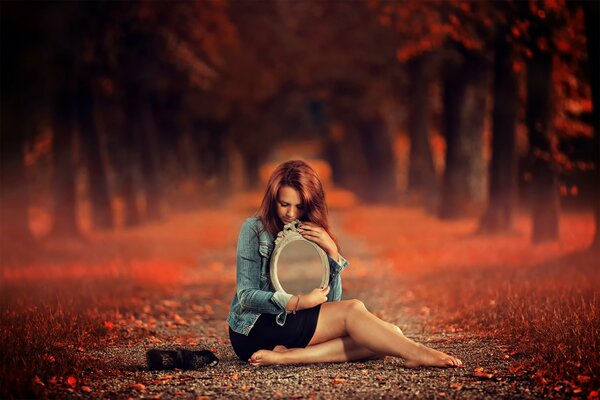 A girl with a mirror sitting along an autumn path