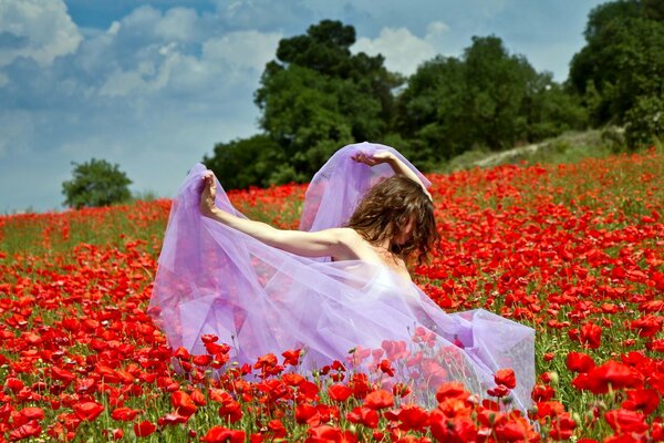 A girl in a flying dress in a meadow with poppies