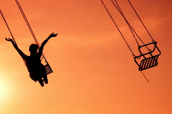 Ragazza sull attrazione con le mani alzate sullo sfondo del tramonto