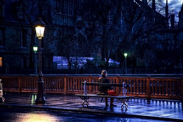 A man sits on a bench under a street lamp in Paris