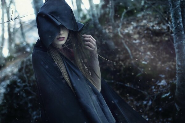 A girl in a black hood in the middle of the forest