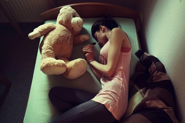 The girl is lying on the bed with a soft toy