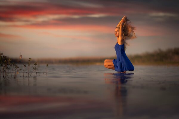 Chica con vestido azul al atardecer en la orilla del lago