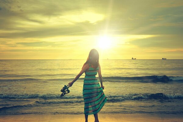Chica en un vestido en la playa en el fondo de la puesta de sol