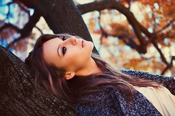 Una mujer con una mirada melancólica se apoya en un árbol