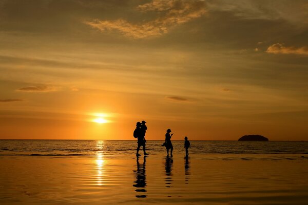 Siluetas de la familia en el fondo de la puesta de sol y el mar