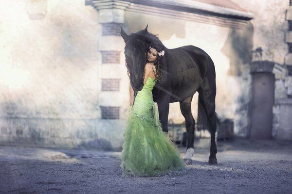 Morena chica en un exuberante vestido verde con una flor en el pelo abraza a un caballo