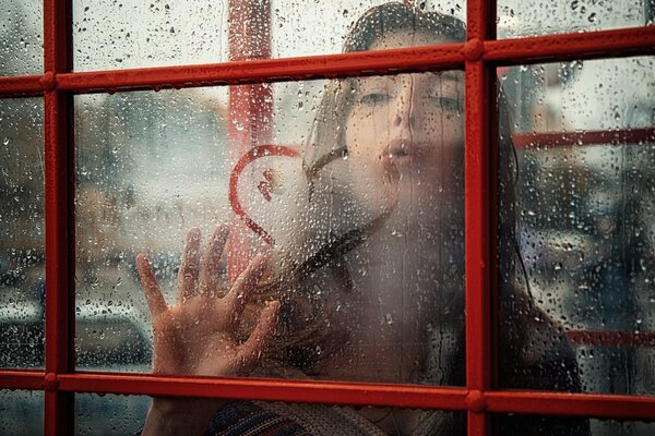 Ein Mädchen zeichnet ein Herz auf ein beschlagenes Fenster