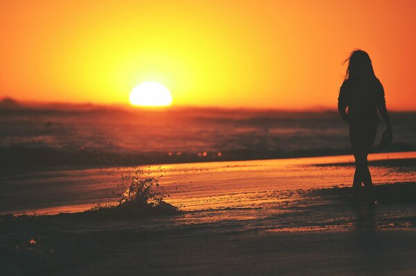 Chica en la orilla del mar en el chorro de la puesta de sol