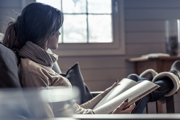The girl is sitting in an armchair and reading a magazine