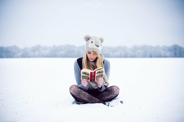 A girl in a hat reads a book in the snow