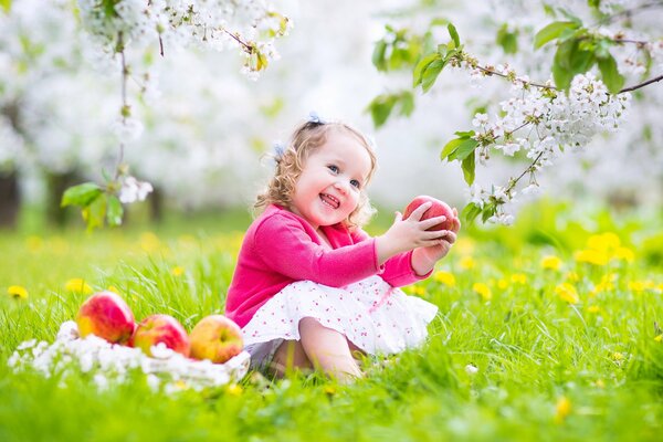 Radosne dziecko z jabłkiem w rękach siedzi na trawie