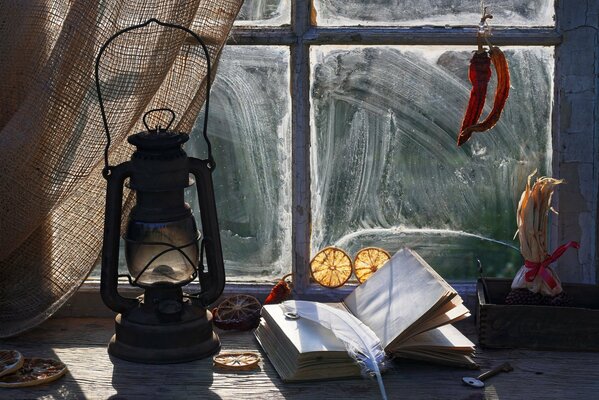 Un livre avec une plume et la lampe à pétrole sur le rebord de la fenêtre
