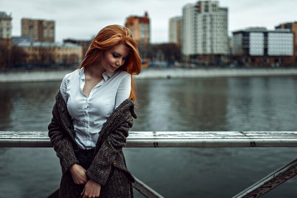 Rudowłosa dziewczyna na moście na tle miasta