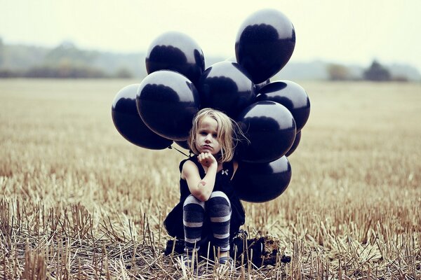 A girl with black balls is sitting on the field