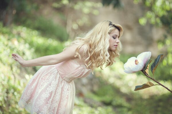 A girl in a soft pink dress sniffs a flower