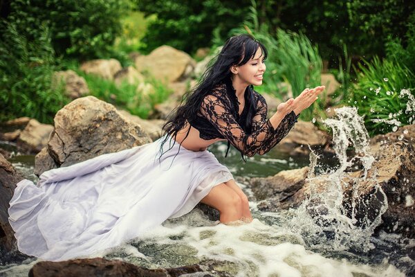 A beautiful girl in the river rejoices in the spray and water