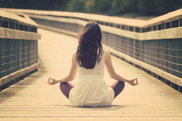 A girl with long hair meditates on a bridge