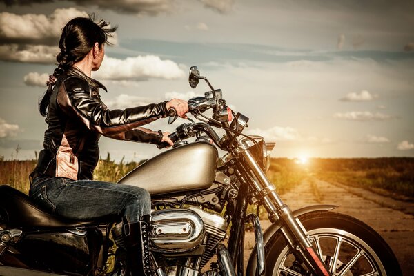 A girl on a motorcycle looks at the sunset