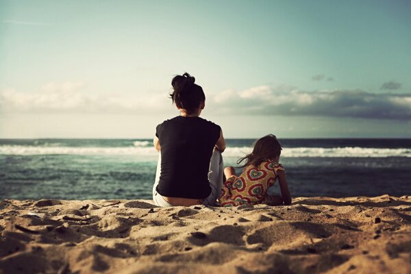 Frau und Mädchen sitzen am Strand