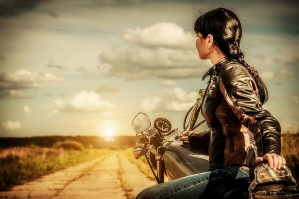 La jeune fille à moto près de la route au coucher du soleil