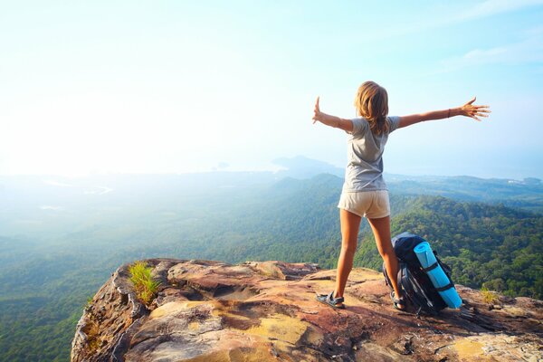 Chica con mochila en un acantilado en las montañas