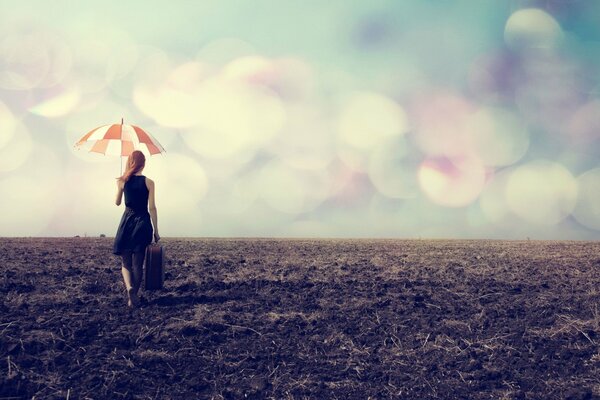 A girl with a suitcase walks through a dusty field under an umbrella