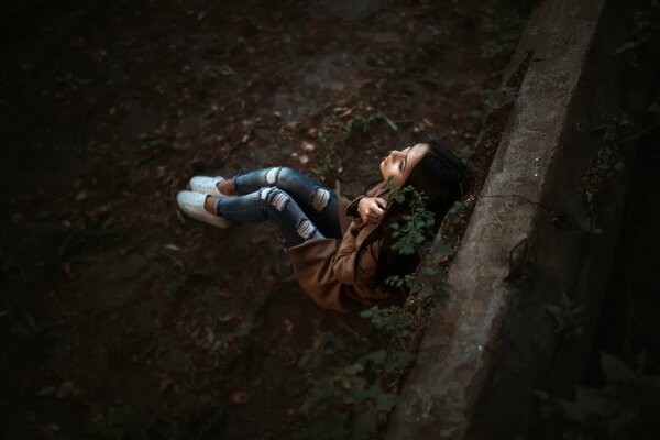 A girl in jeans is sitting on the ground