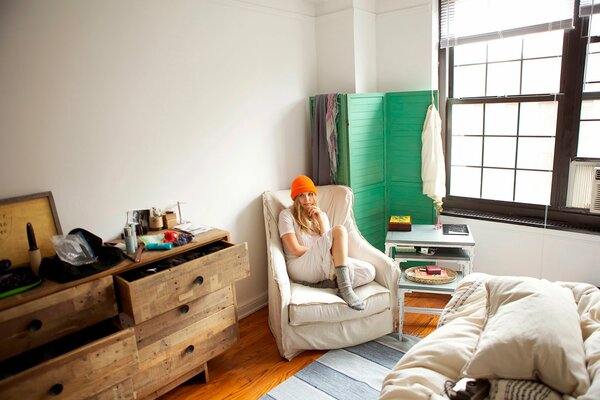 Elizabeth Olsen is sitting in the room in an orange hat on a chair