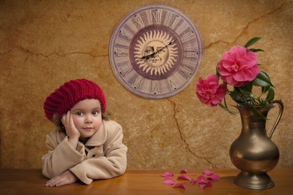 Ein kleines Mädchen in einer rosa Baskenmütze sitzt mit Pfingstrosen am Tisch