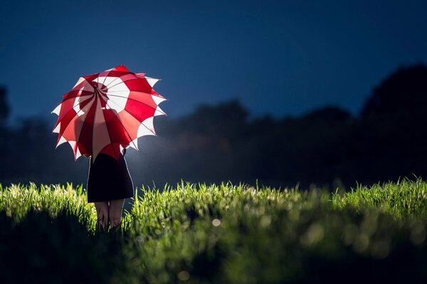 A girl with a red and white umbrella in the grass at night