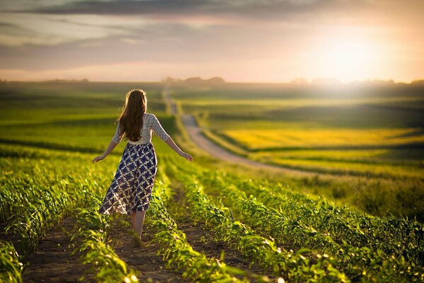 A girl walks through a field in the distance the sun is setting