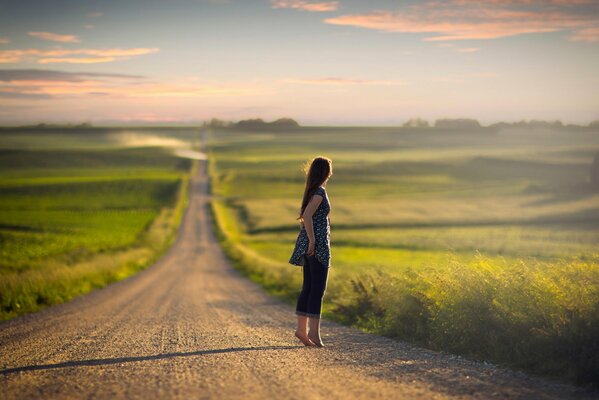 A girl in jeans and barefoot is standing on the road