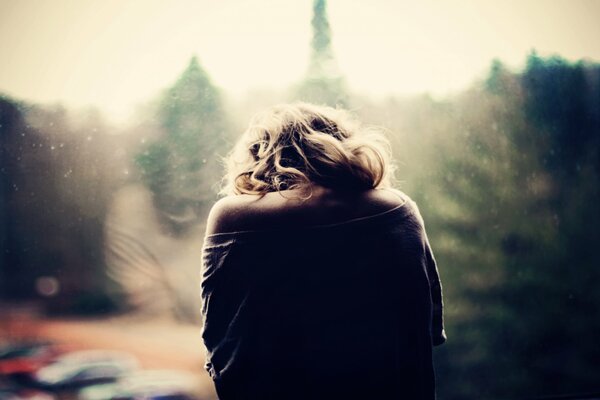 The girl is sitting at the window with a sad mood, looking at the city