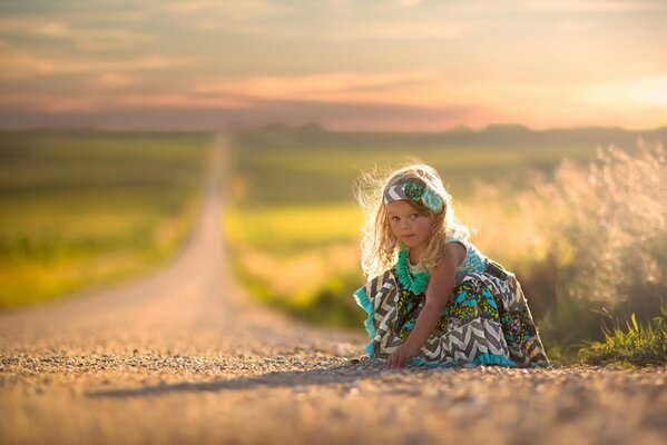 A little girl in a dress sitting on the road