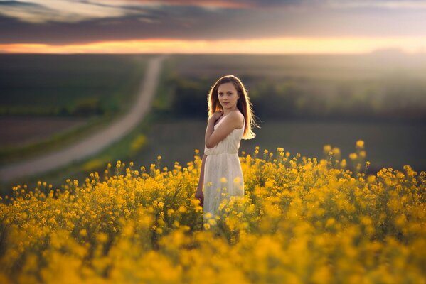 A girl in a field in flowers and a road going into the distance