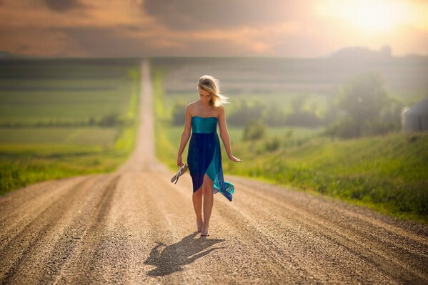 A girl walks alone on a dusty road barefoot