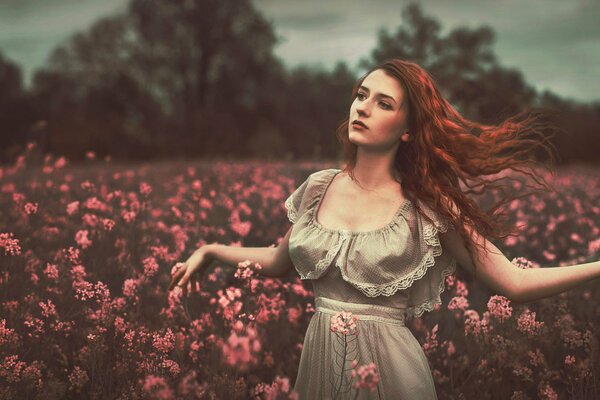 Rudowłosa dziewczyna z eleganckimi lokami na polu z kwiatami