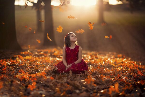 Chica sentado hojas de naranja se regocija en el otoño