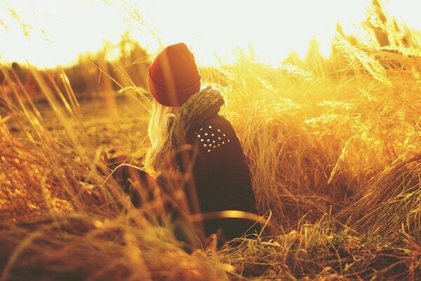 A girl in a hat is sitting in a field