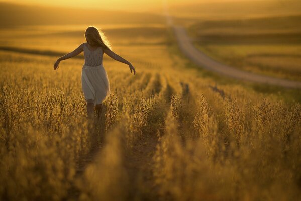 Das Mädchen läuft mit ausgestreckten Händen unter der untergehenden Sonne über das Feld und in die Ferne geht der Weg